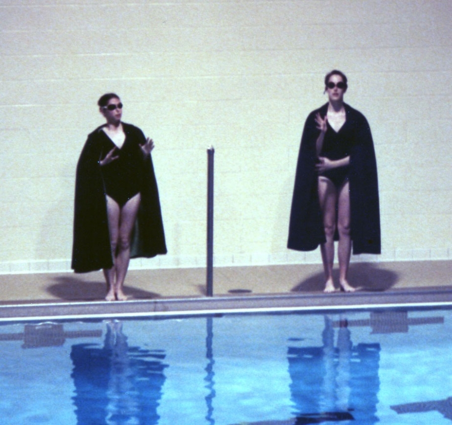 two synchro swimmers in capes stand by a pool